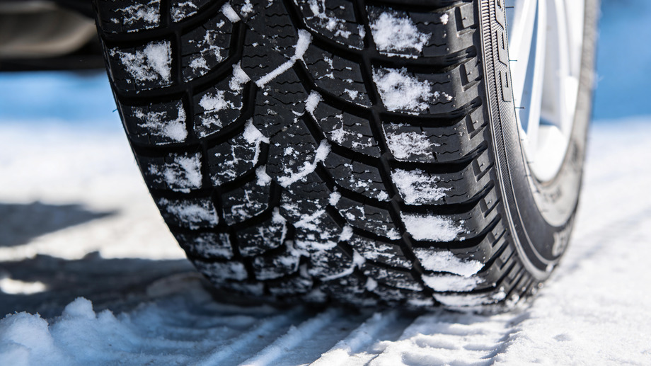 Close-up shot of a winter car tire tread on fresh white snow showing safety features.