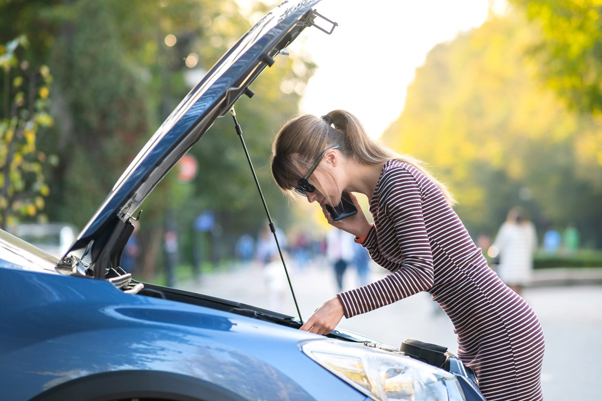 Girl talking on the phone with the hood of her car open