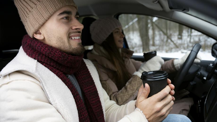 A cozy car interior with a hot drink on the dashboard against a snowy park background.