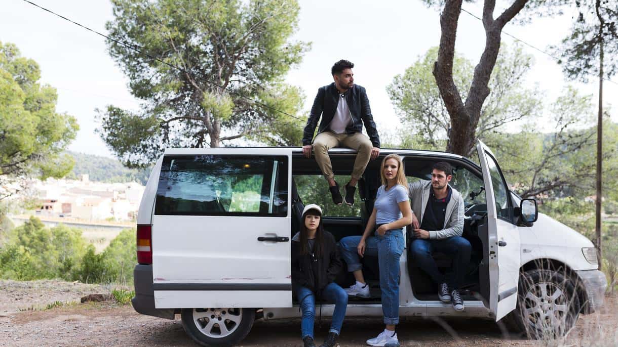 A group of young people or a family with teenagers is relaxing in an open minivan in nature.