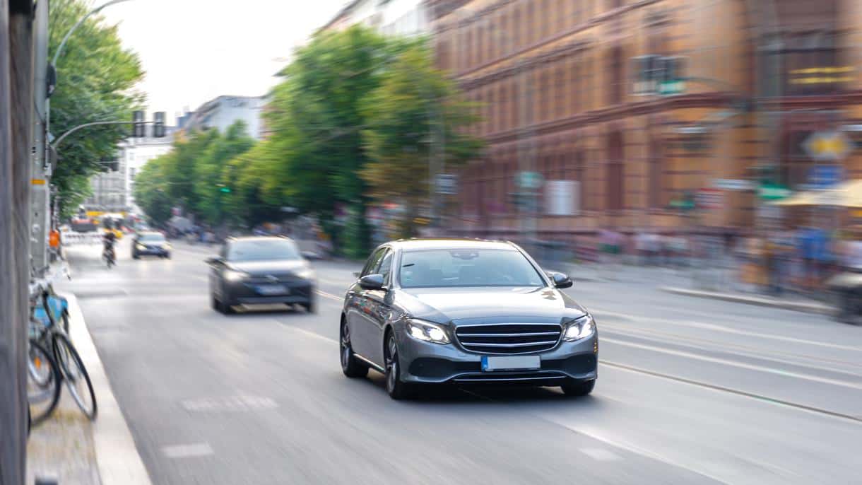 A grey business class sedan drives along a city street, a comfortable car for long-distance trips.