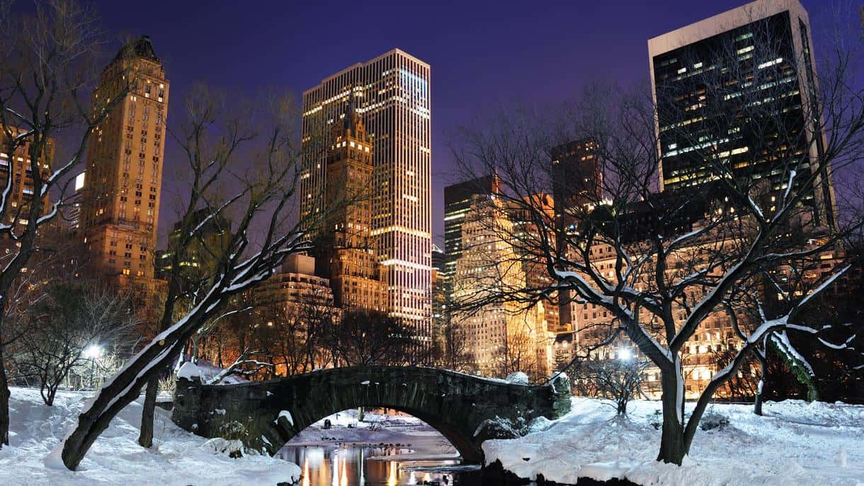 Winter night view of Central Park in New York with the illuminated skyline and Gapstow Bridge covered in snow