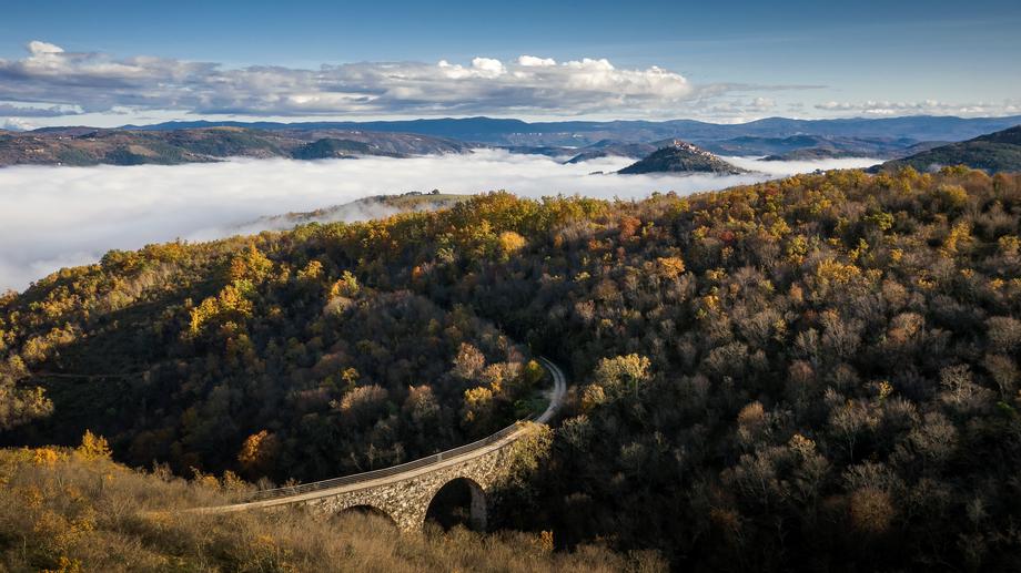 A winding bridge across an autumn forest in a misty mountain valley, symbolizing a scenic route for traveling by car.